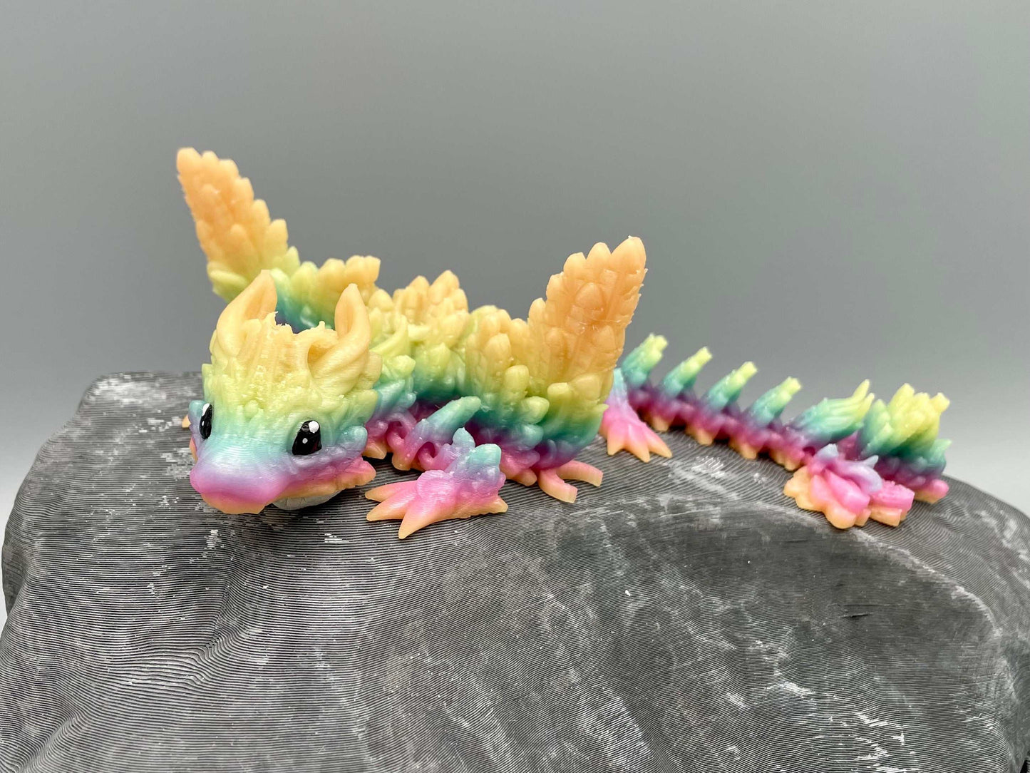 Leuchtender geflügelter Baby Mond Drache in Regenbogenfarben